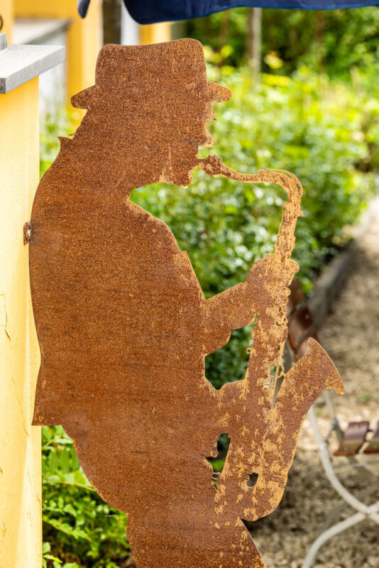 Rostfarbene Metallskulptur eines Saxophonspielers im Biergarten des Landhaus Begatal