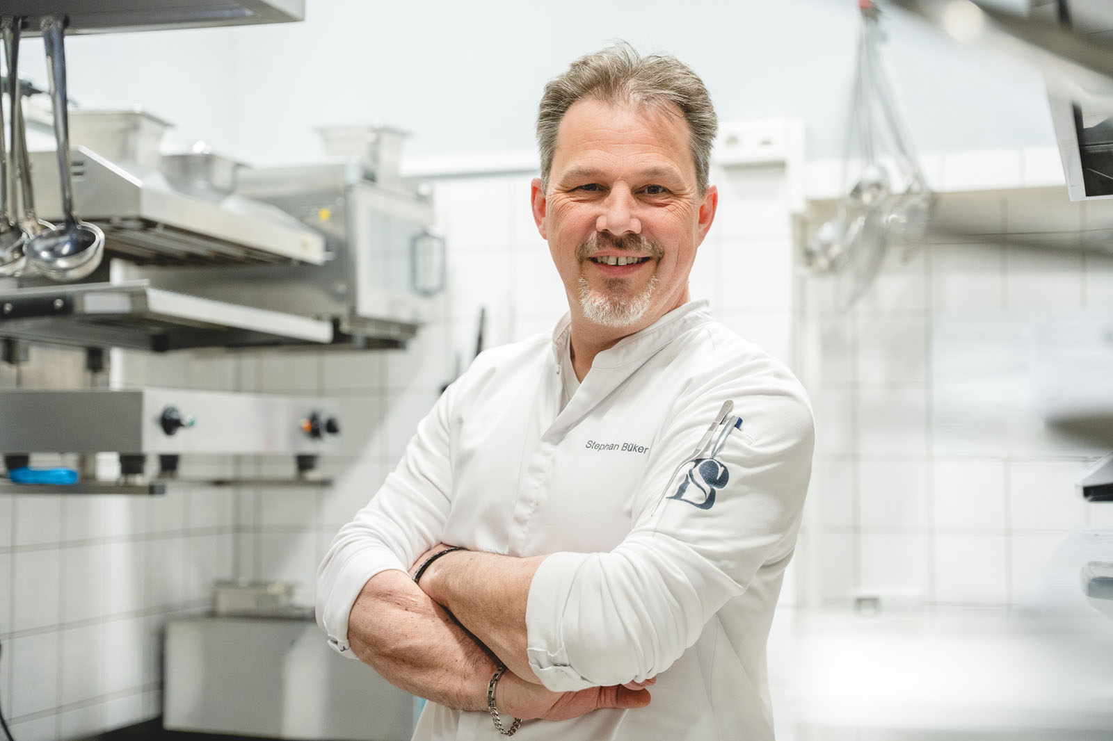 Küchenchef Stephan Büker mit verschränkten Armen in weißer Kochjacke in der Küche des Landhaus Begatal
