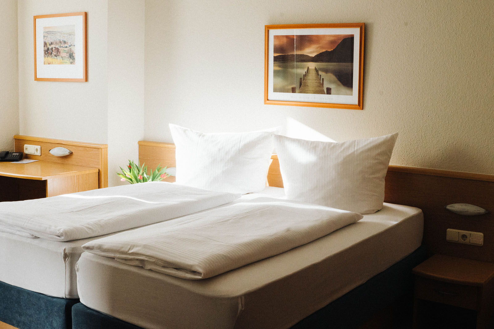 Gepflegtes Doppelzimmer im Hotel Landhaus Begatal mit frisch bezogenen Betten, Holzmöbeln und Tulpenstrauß