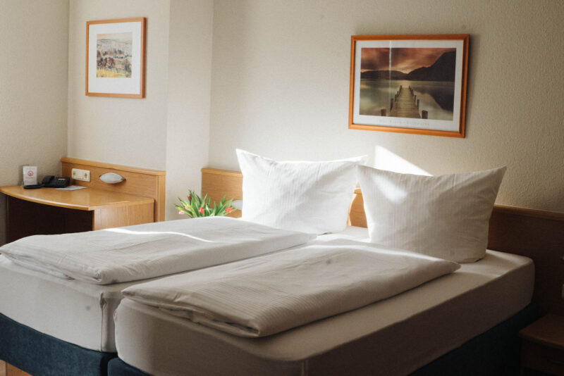 Helles Doppelzimmer im Hotel Landhaus Begatal mit frisch bezogenen Betten, Holzmöbeln und Tulpenstrauß am Kopfende