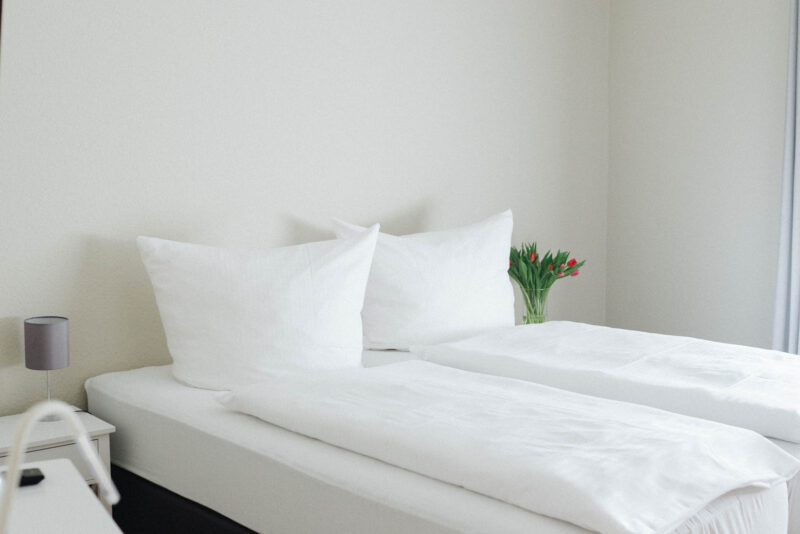 Hell eingerichtetes Einzelzimmer im Hotel Landhaus Begatal mit frisch bezogenem Bett und Tulpen auf dem Nachttisch