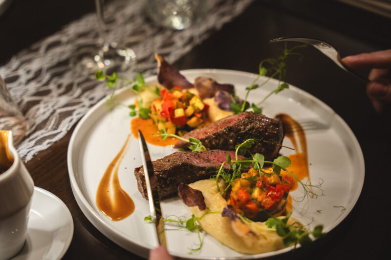 Aufgeschnittenes Rinderfilet medium-rare mit Gemüsesalsa, Kartoffelcreme und Jus auf weißem Teller im Landhaus Begatal
