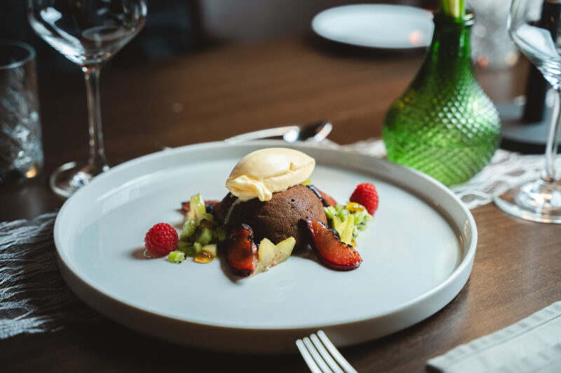 Schokoladenküchlein mit Vanilleeis, Himbeeren und frischen Früchten auf einem weißen Teller im Restaurant.