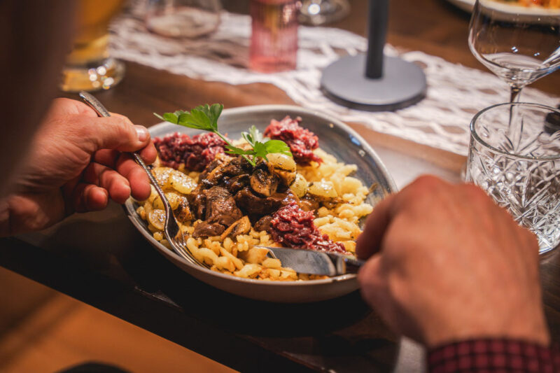 Herzhafter Teller mit Spätzle, Rindfleisch, Pilzen, Zwiebeln und Rotkohl am gedeckten Tisch.